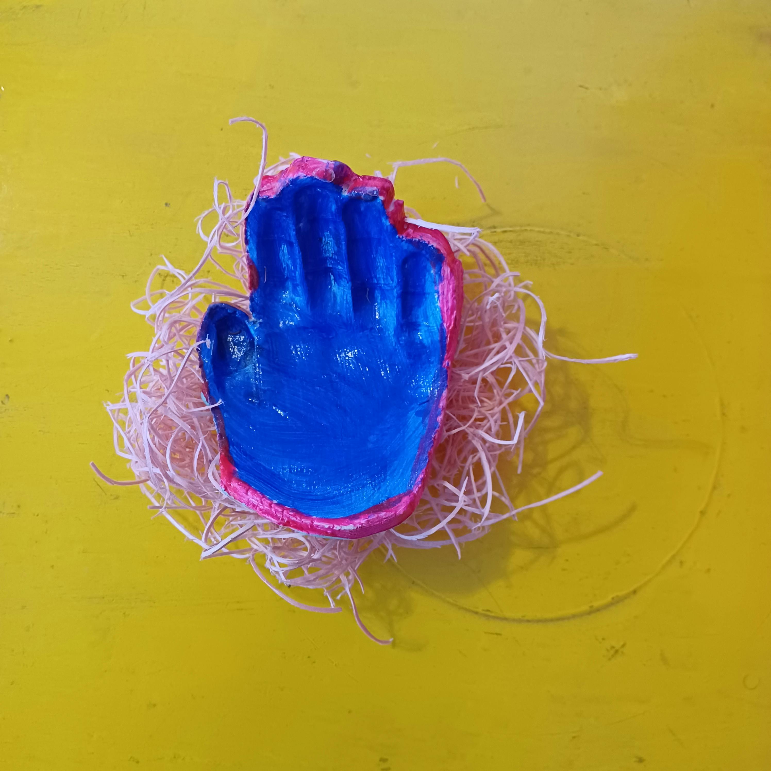 Blue hand-shaped object with pink trim on a bed of white shredded material