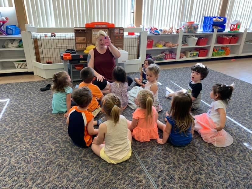 Person speaking to a group of children sitting on the floor in a classroom