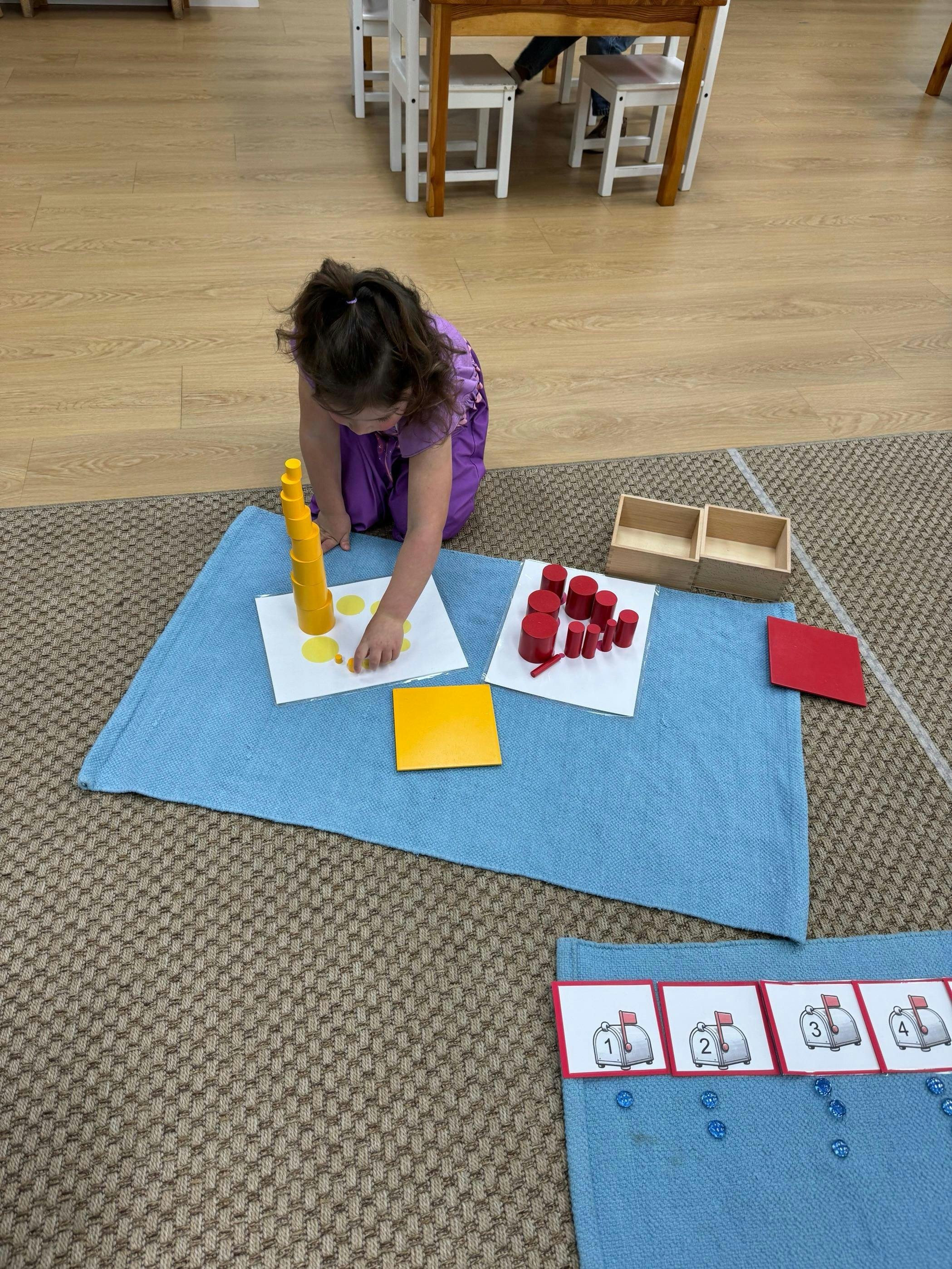 Child kneeling on the floor, playing with yellow and red cylindrical blocks
