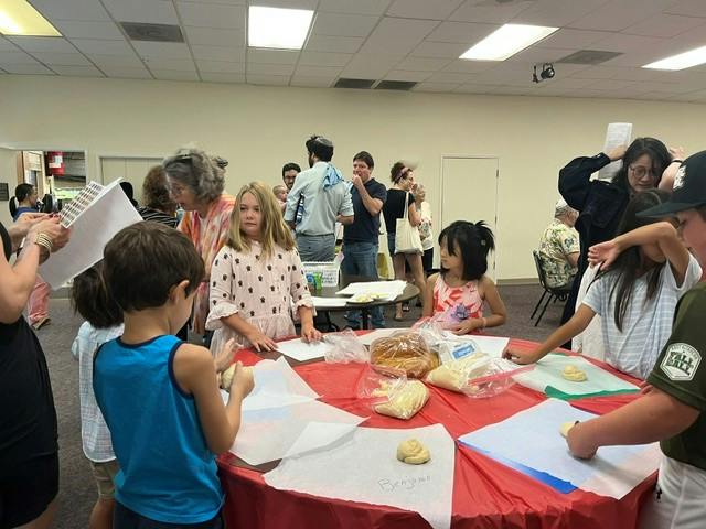 People gathered around tables shaping dough in a community room