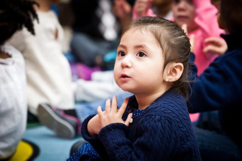 Child looking up with clasped hands in a classroom setting