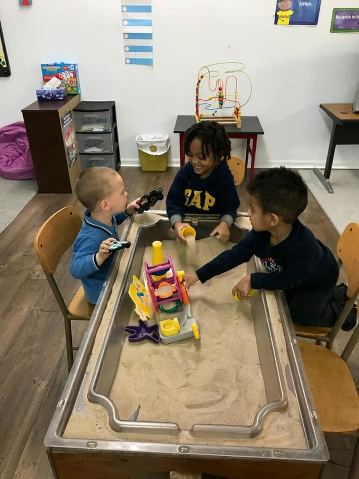 Three children playing with toys in a sand table