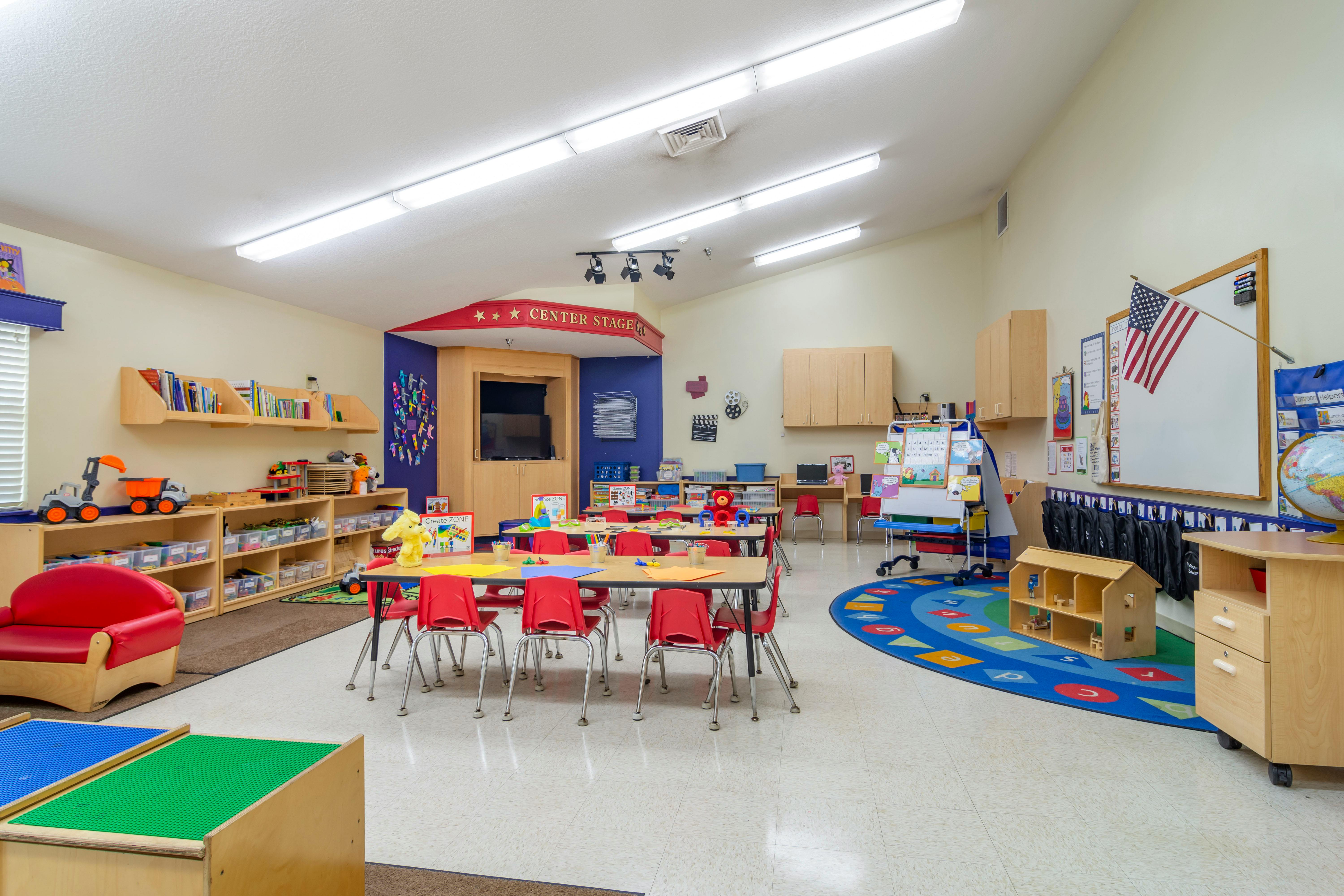 Classroom with small tables, red chairs, bookshelves, and a 'Center Stage' area