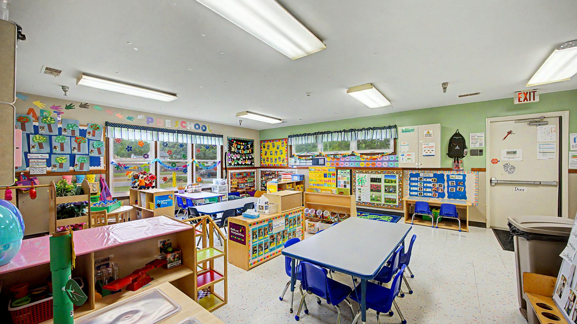 A colorful preschool classroom with small tables, chairs, and learning displays