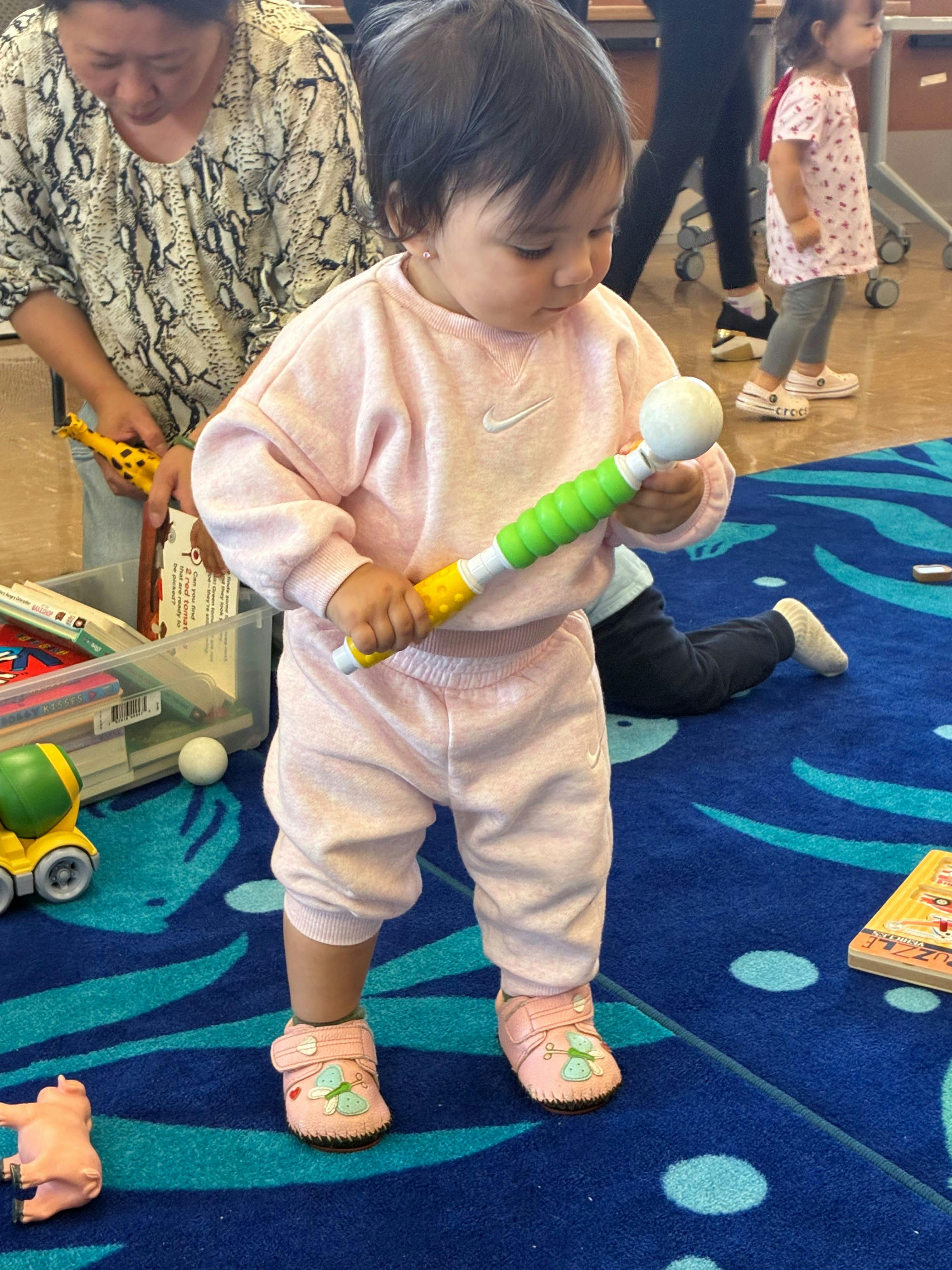 Child standing on a blue rug and playing with a toy rattle