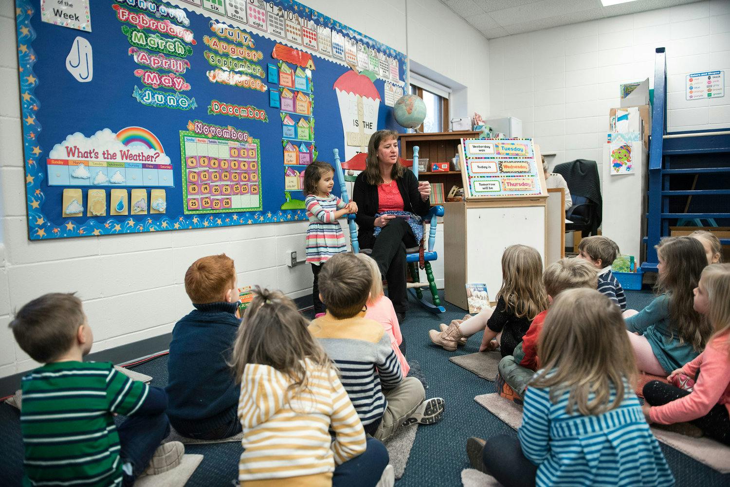 Adult and child speaking to a group of children sitting on the floor in a classroom