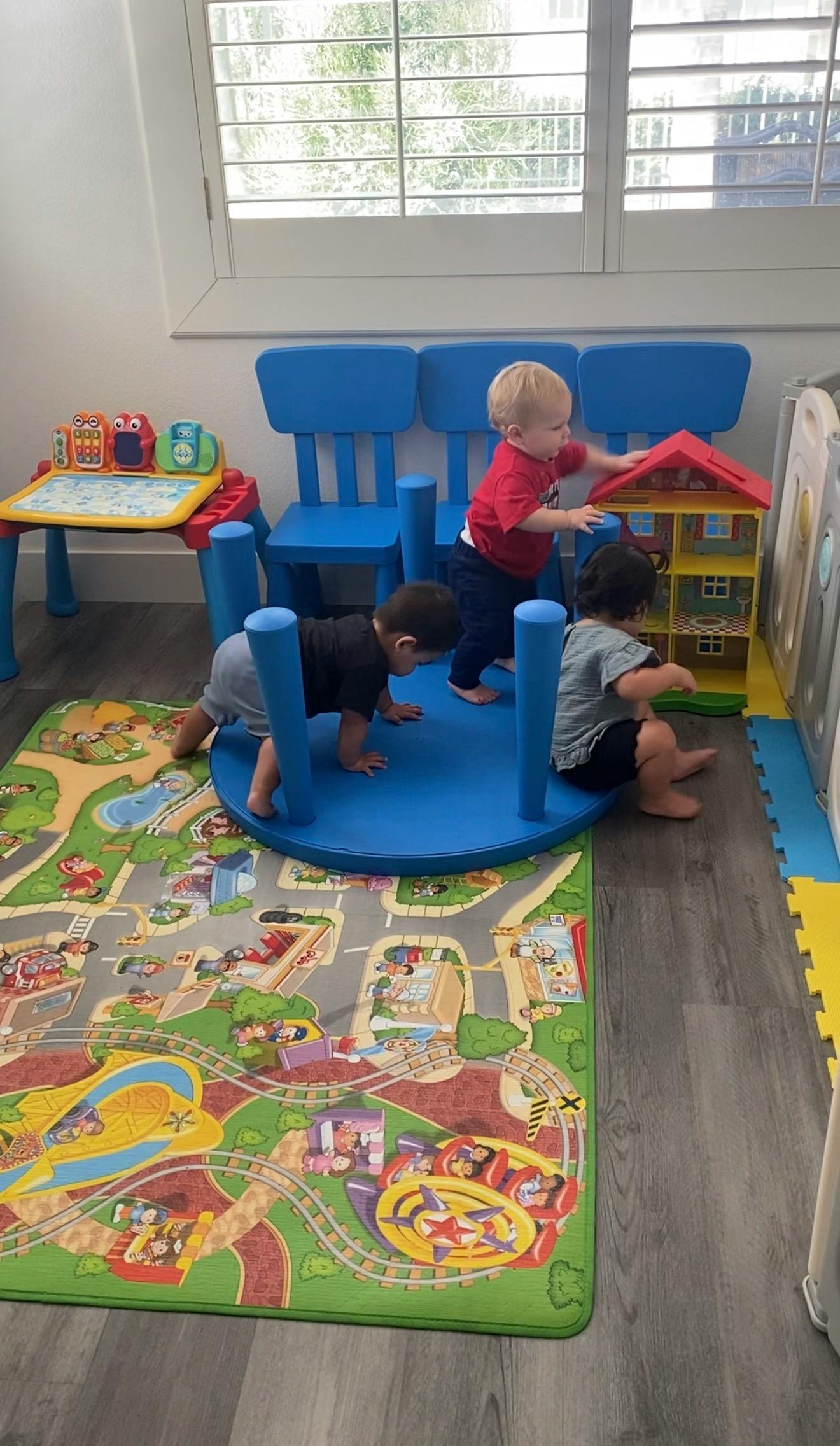 Three children playing on a rug with toys in a room