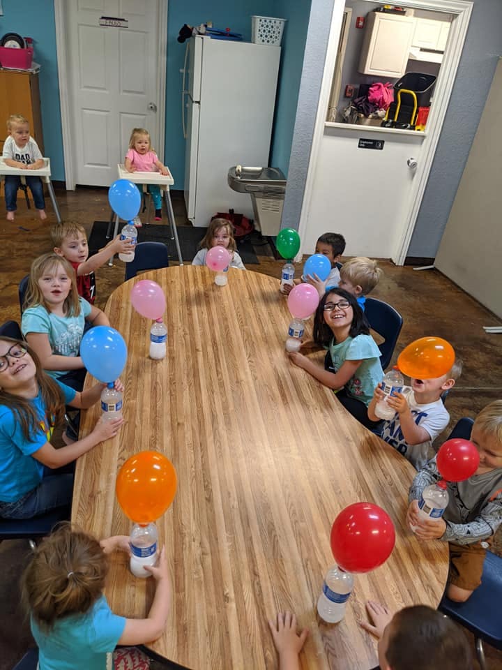 Children sitting around a table with balloons attached to water bottles