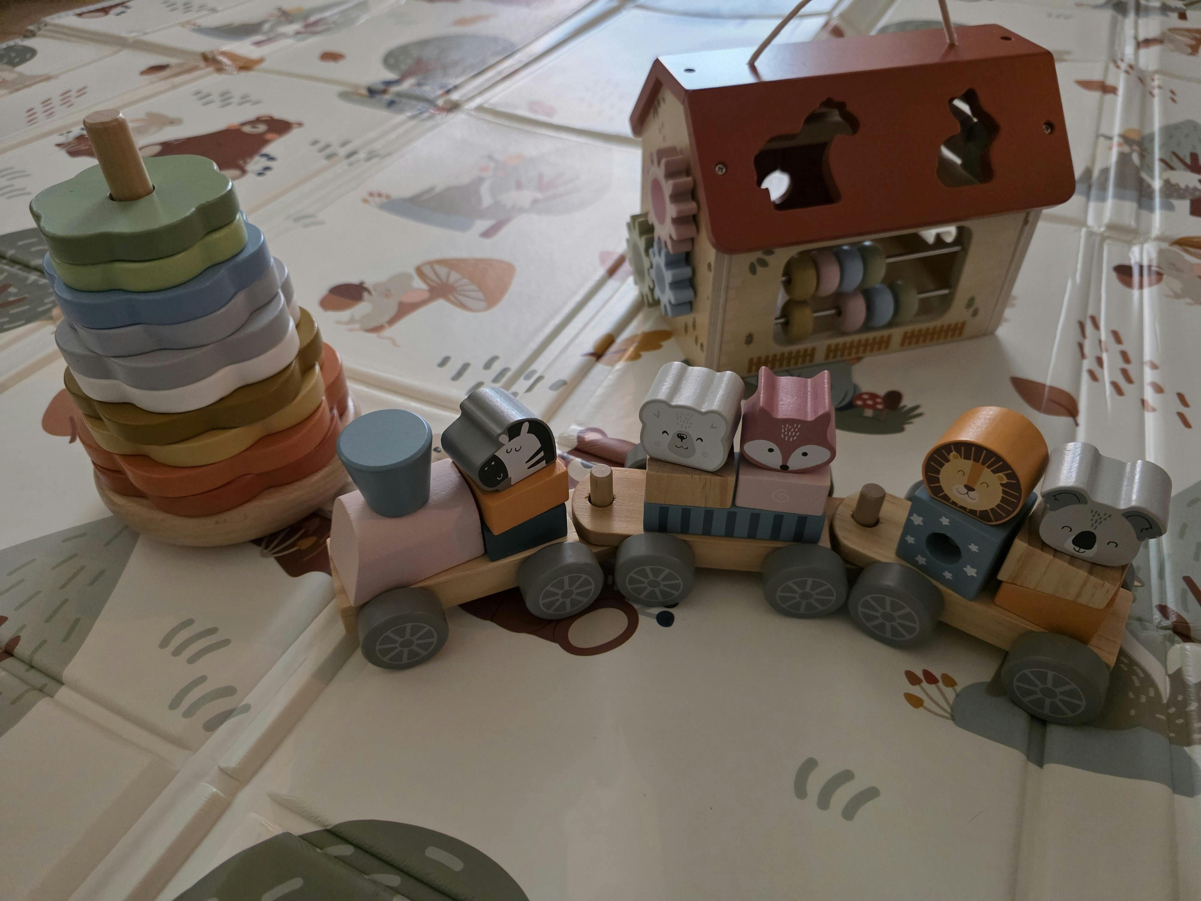 Wooden toy train, stacking ring toy, and house shape sorter on a play mat