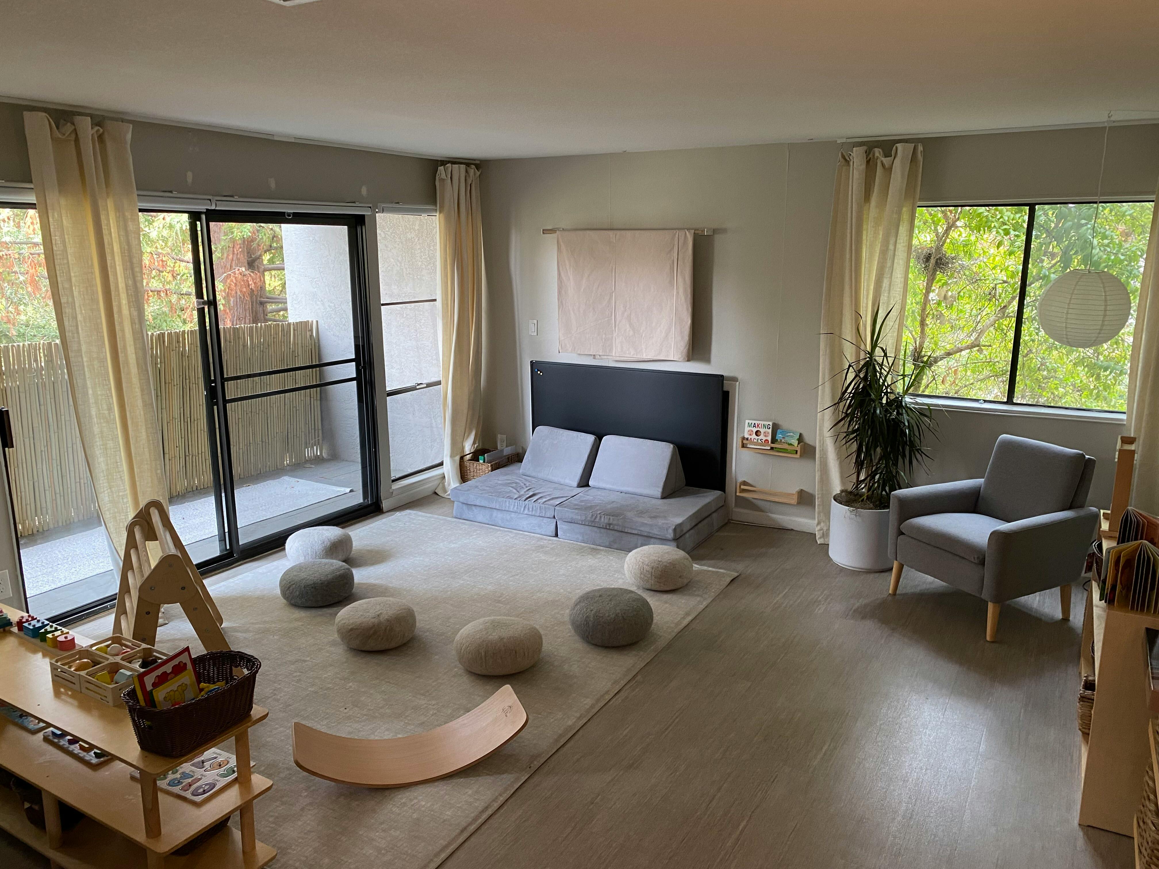 Room with floor cushions, a low bed, and large windows