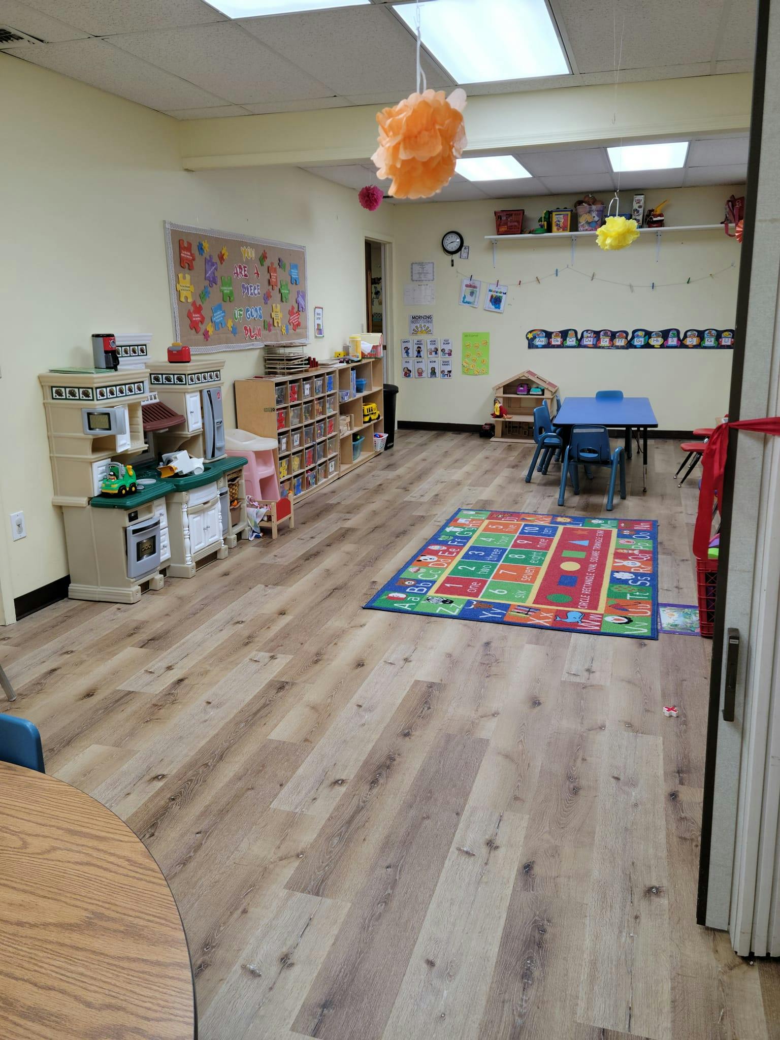 Playroom with toy kitchen, bookshelves, small table and chairs, and colorful rug