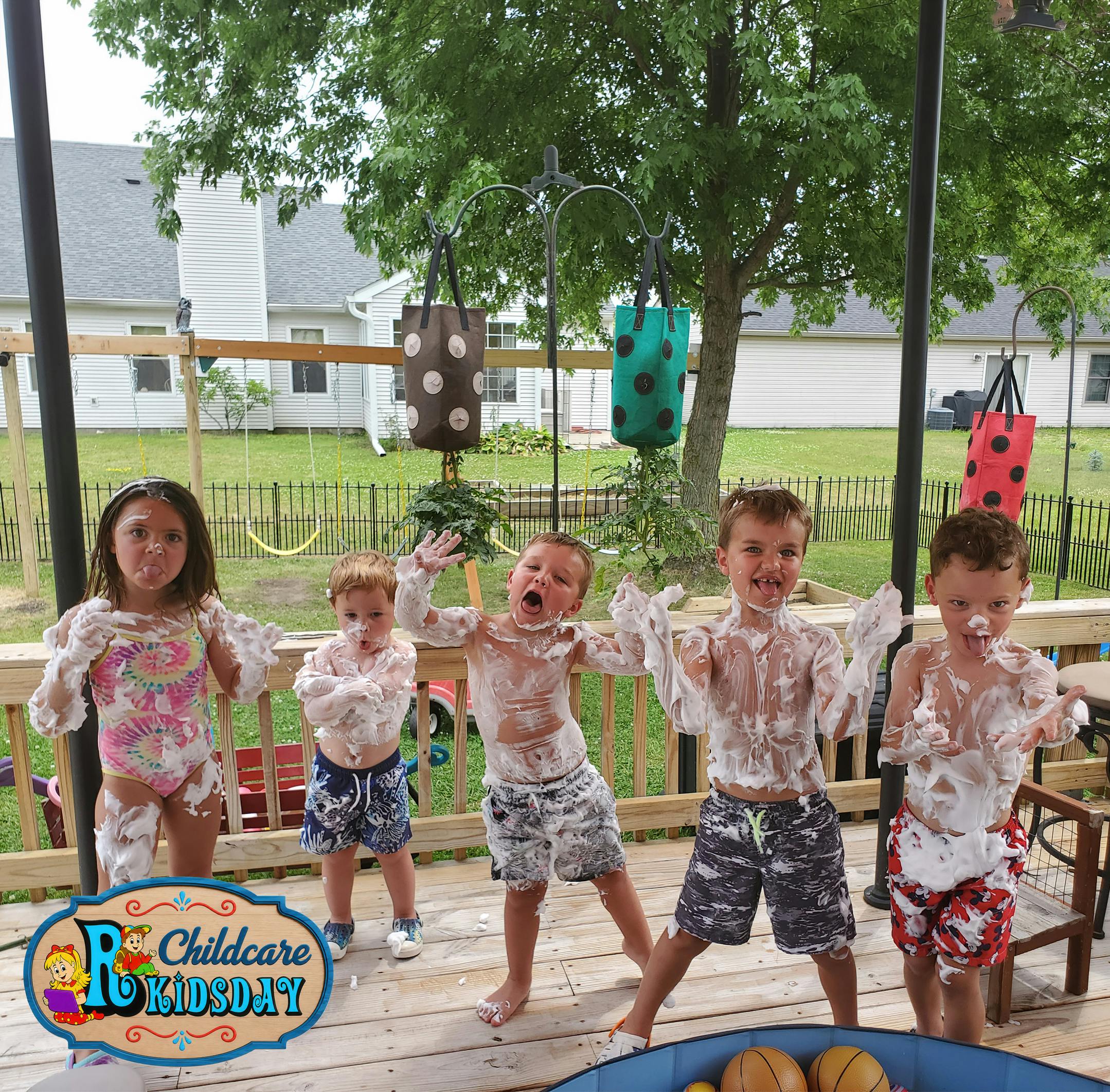 Five children covered in white foam playing on a wooden deck