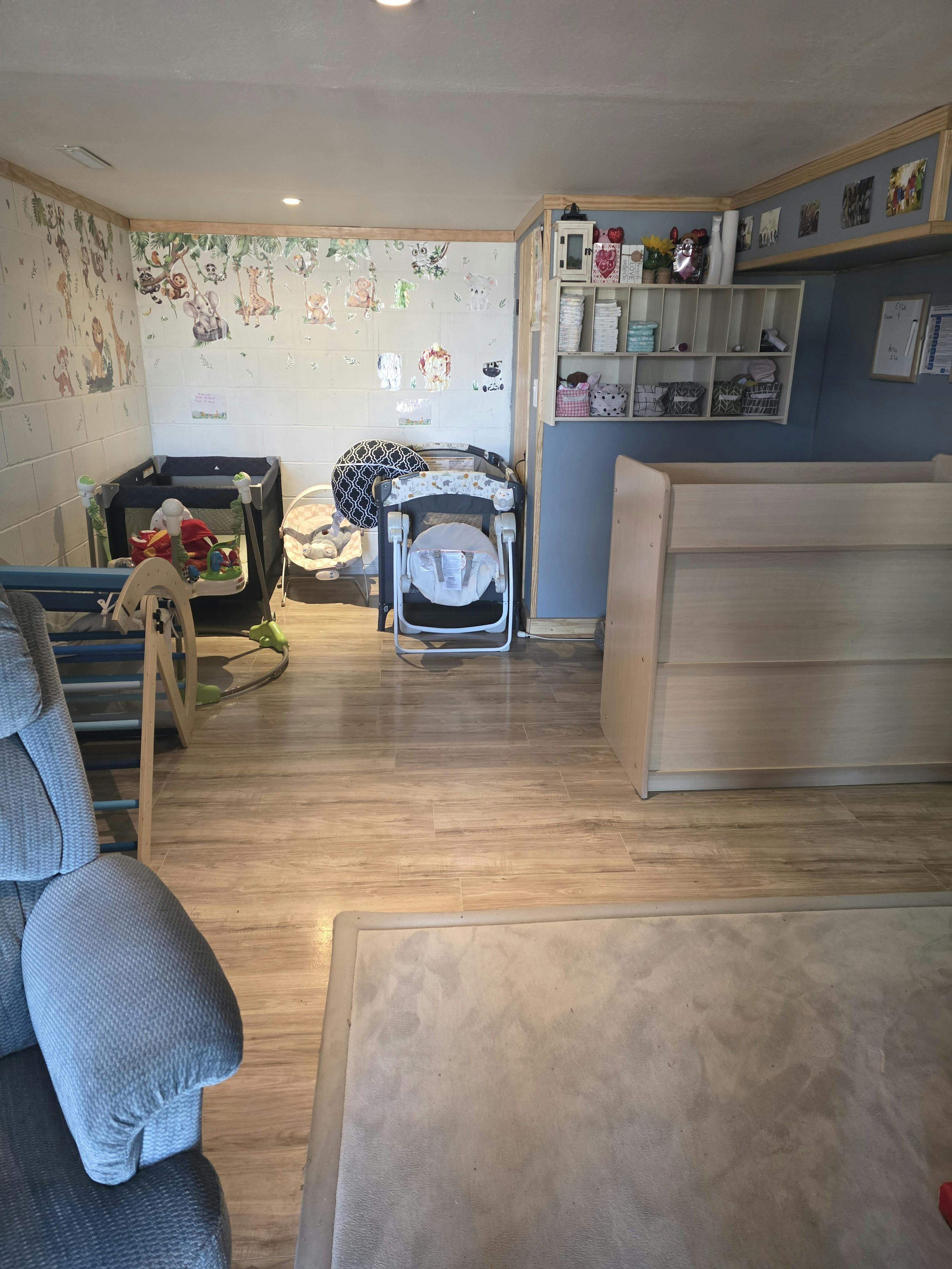 A room with animal wall decals, a playpen, baby swing, and shelving with supplies