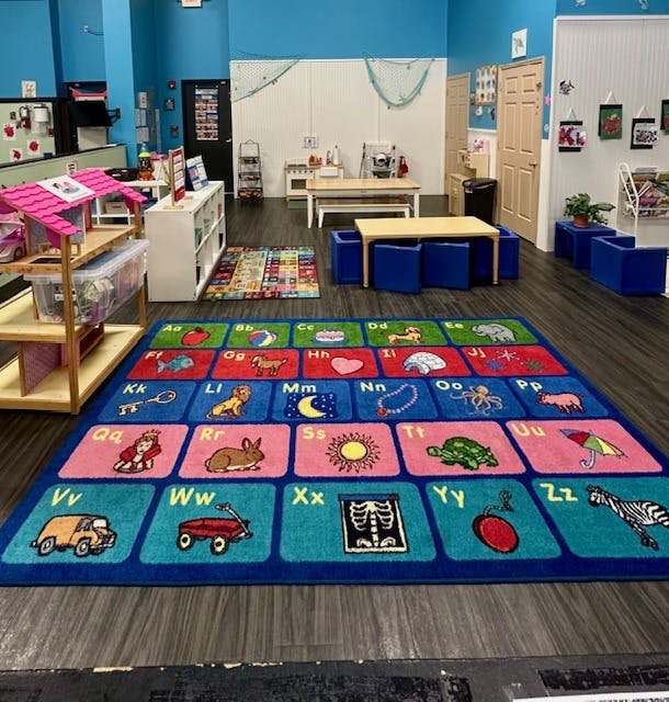 Classroom with an alphabet rug, small tables, and play furniture