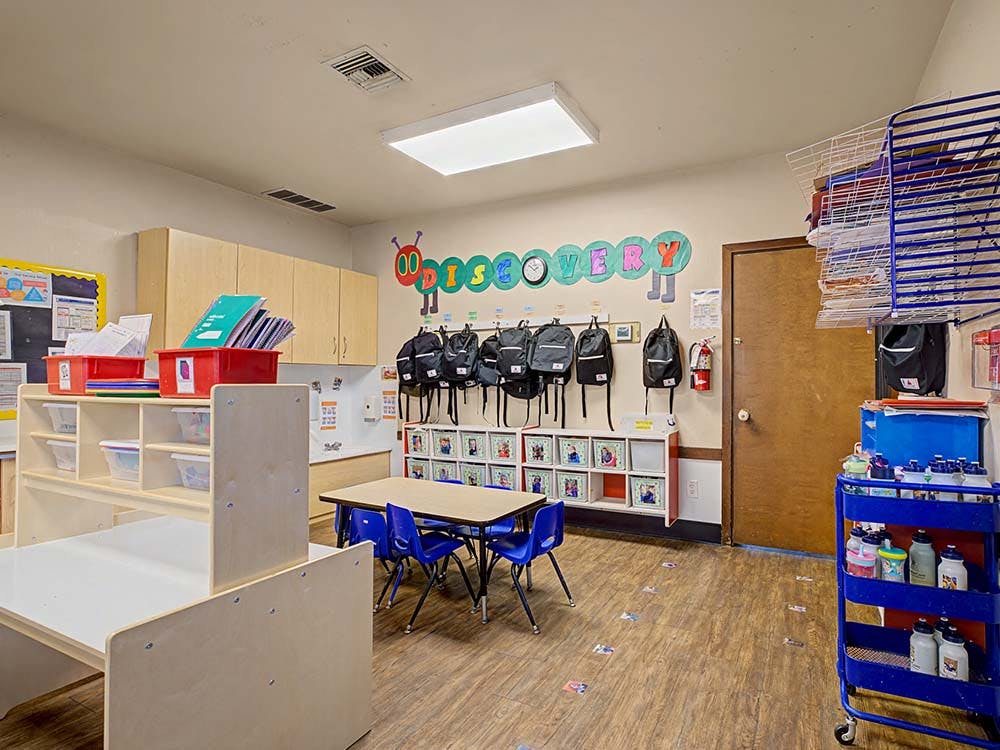 Classroom with child-sized furniture, backpacks, and the word DISCOVERY on the wall