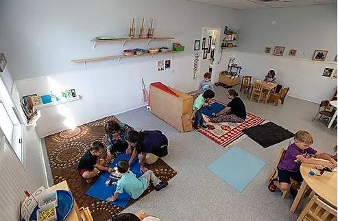 Children and adults playing on rugs in a classroom