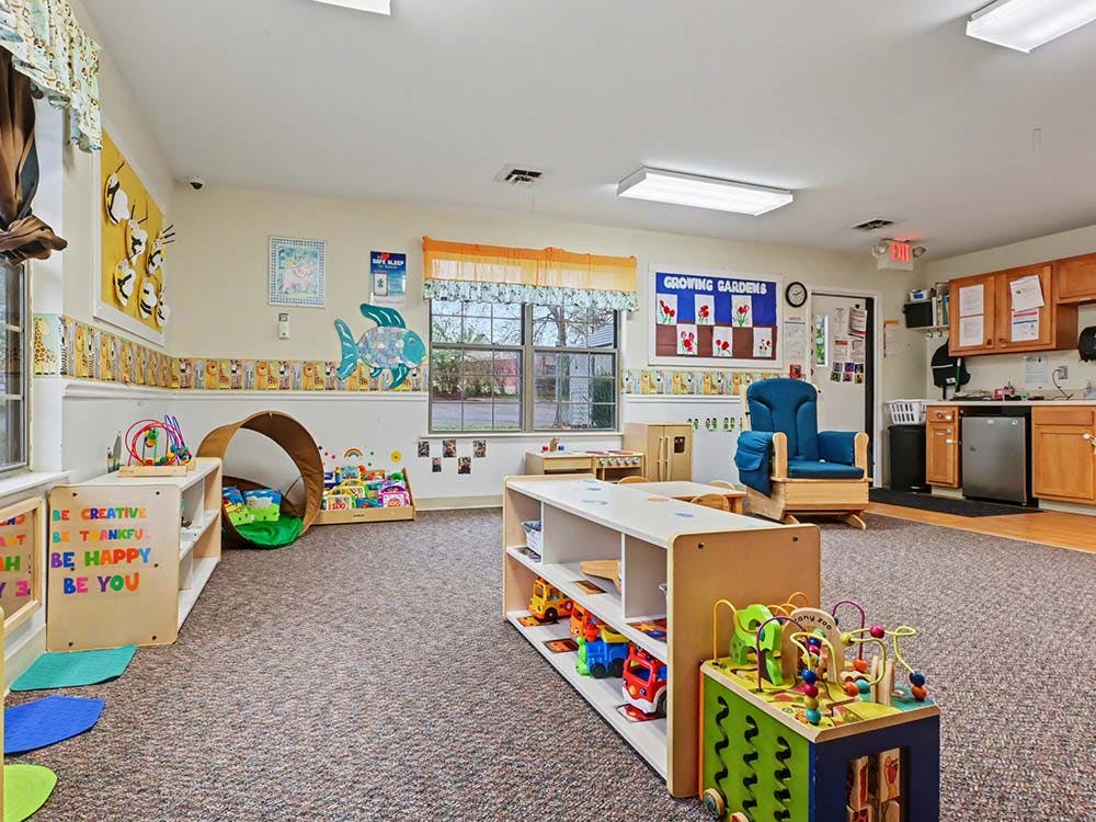 Classroom with shelves of toys, small tables, a tunnel, and a blue rocking chair