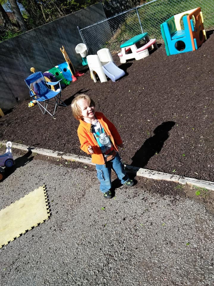 Child standing on playground with wood chips and play equipment