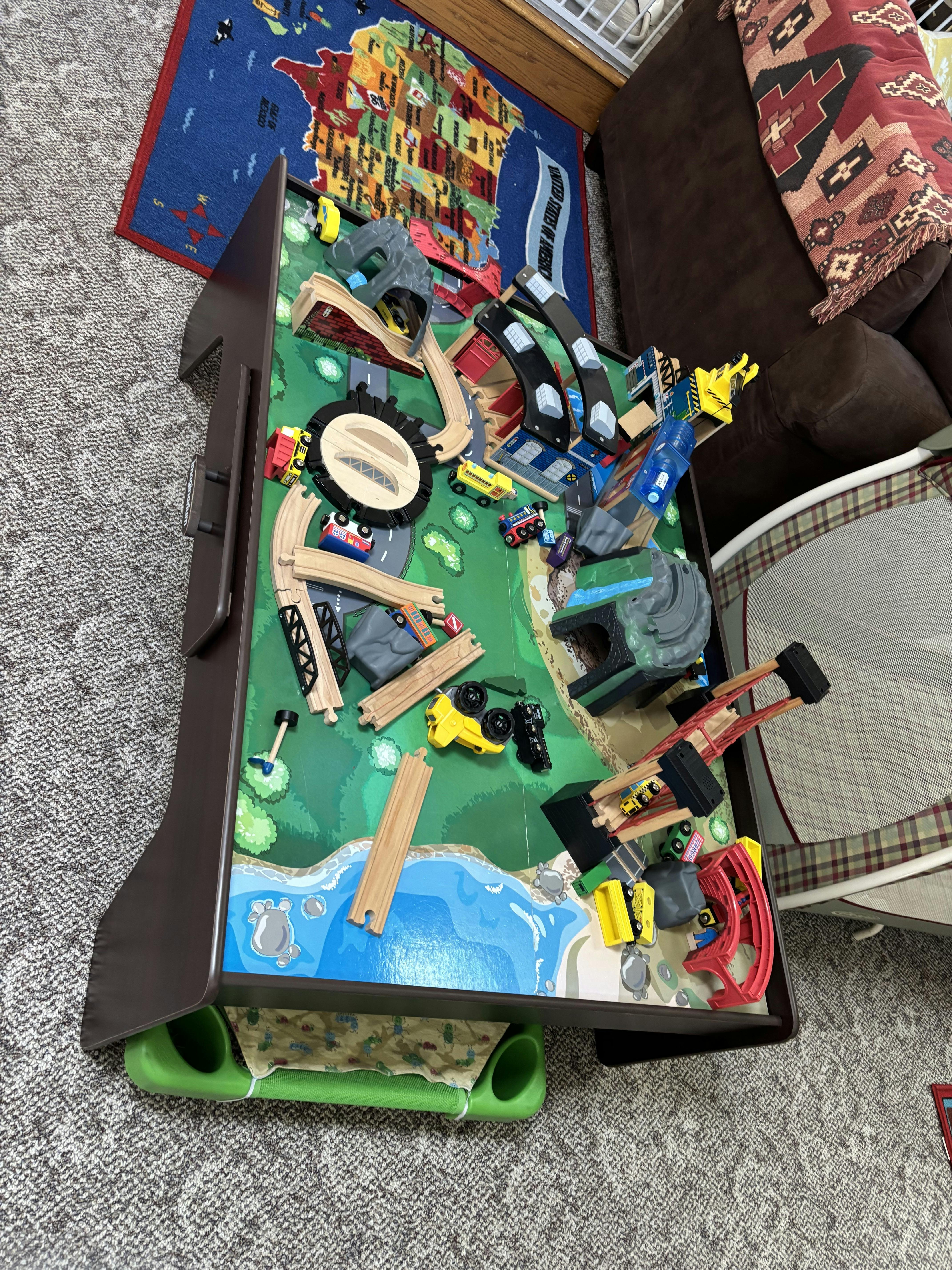 Wooden toy train set on a play table with tunnels and miniature vehicles