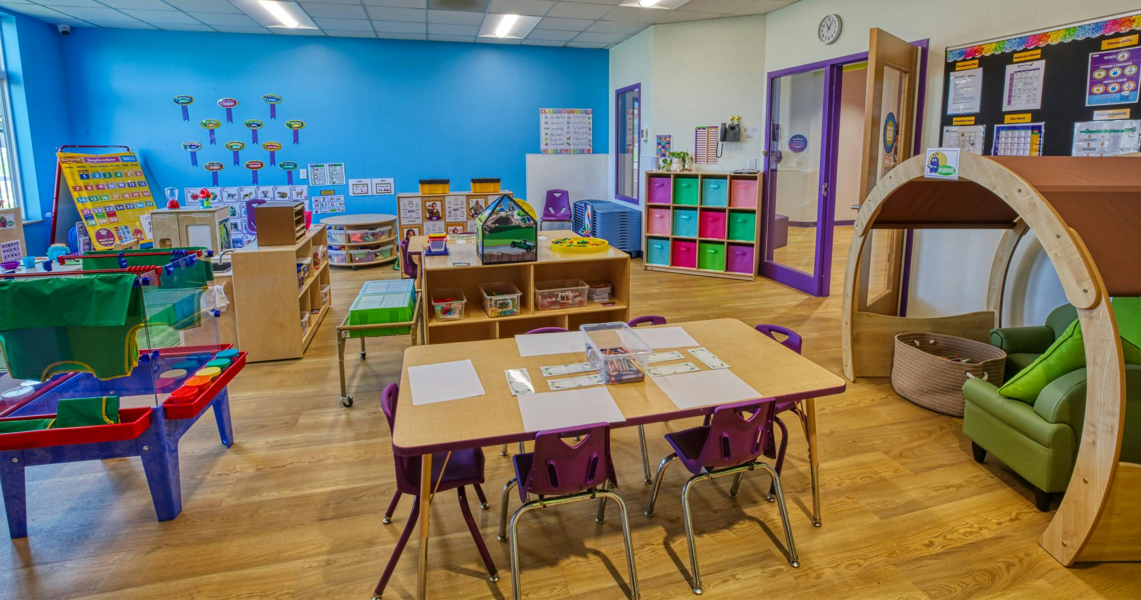 Children's classroom with blue wall, small tables, and play areas
