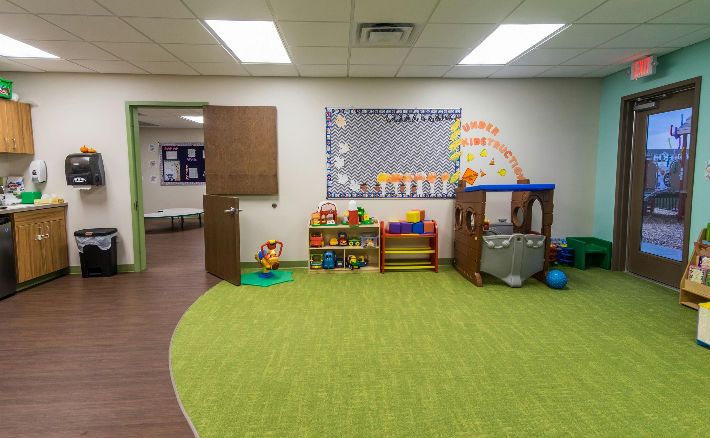 Playroom with green carpet, toys, and a small kitchen area