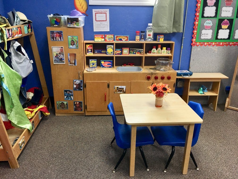 Classroom with small table and chairs, play kitchen, and storage shelves