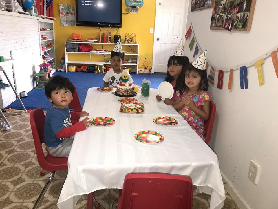 Children wearing party hats sitting at a table with cakes and candy