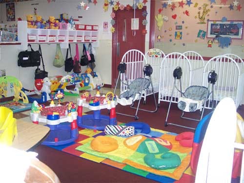 Daycare room with cribs, play mats, and infant activity centers