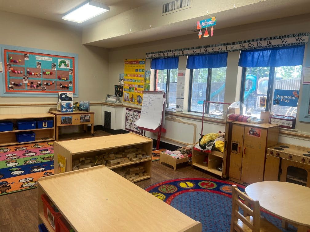 An empty preschool classroom with toys, small tables, and bright rugs