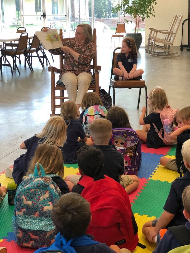 Adult reading a book to a group of children sitting on a colorful mat