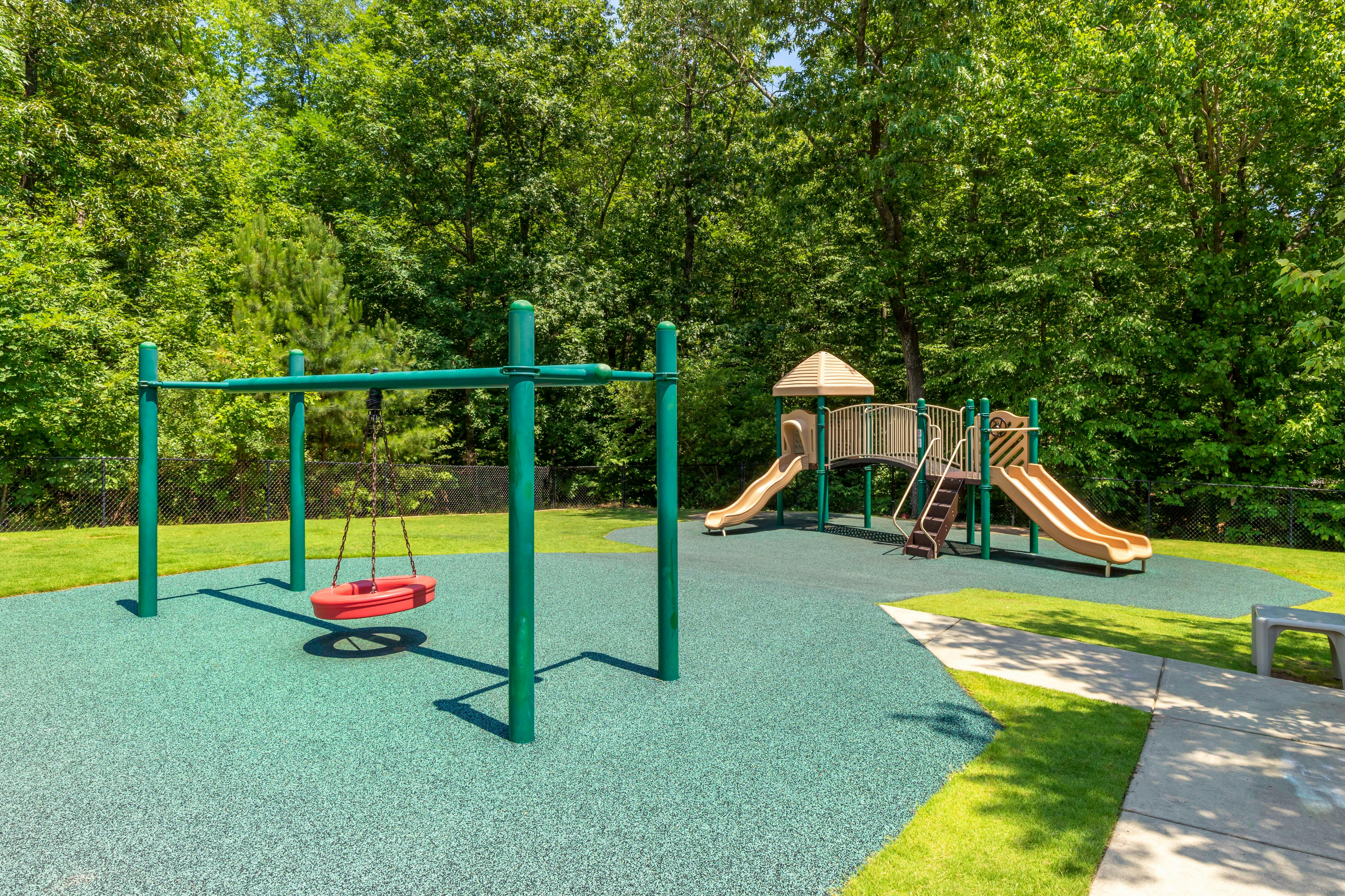 A playground with a red swing, slides, and stairs on a green surface
