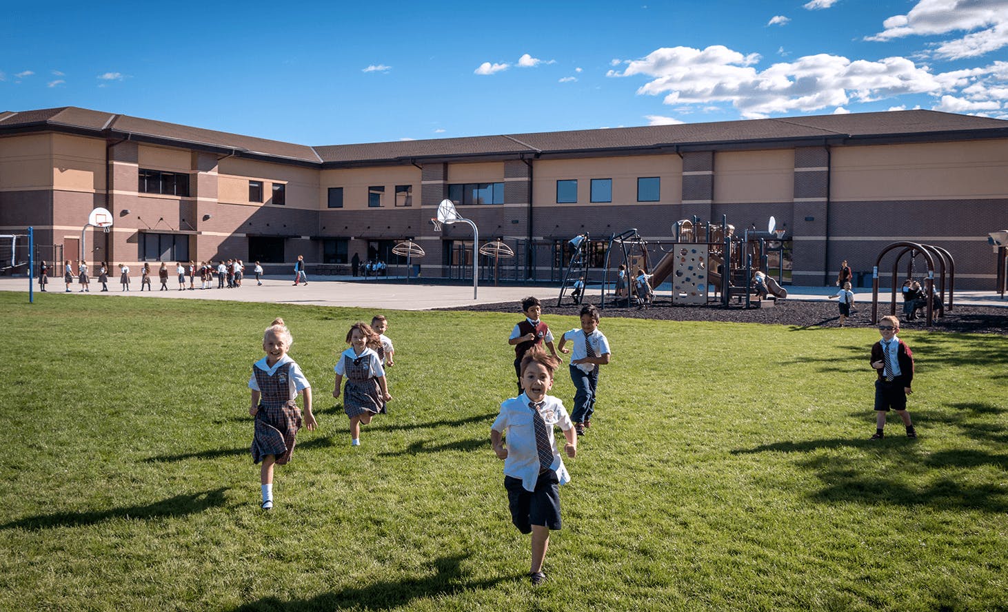 Children running on a grassy field in front of a school building