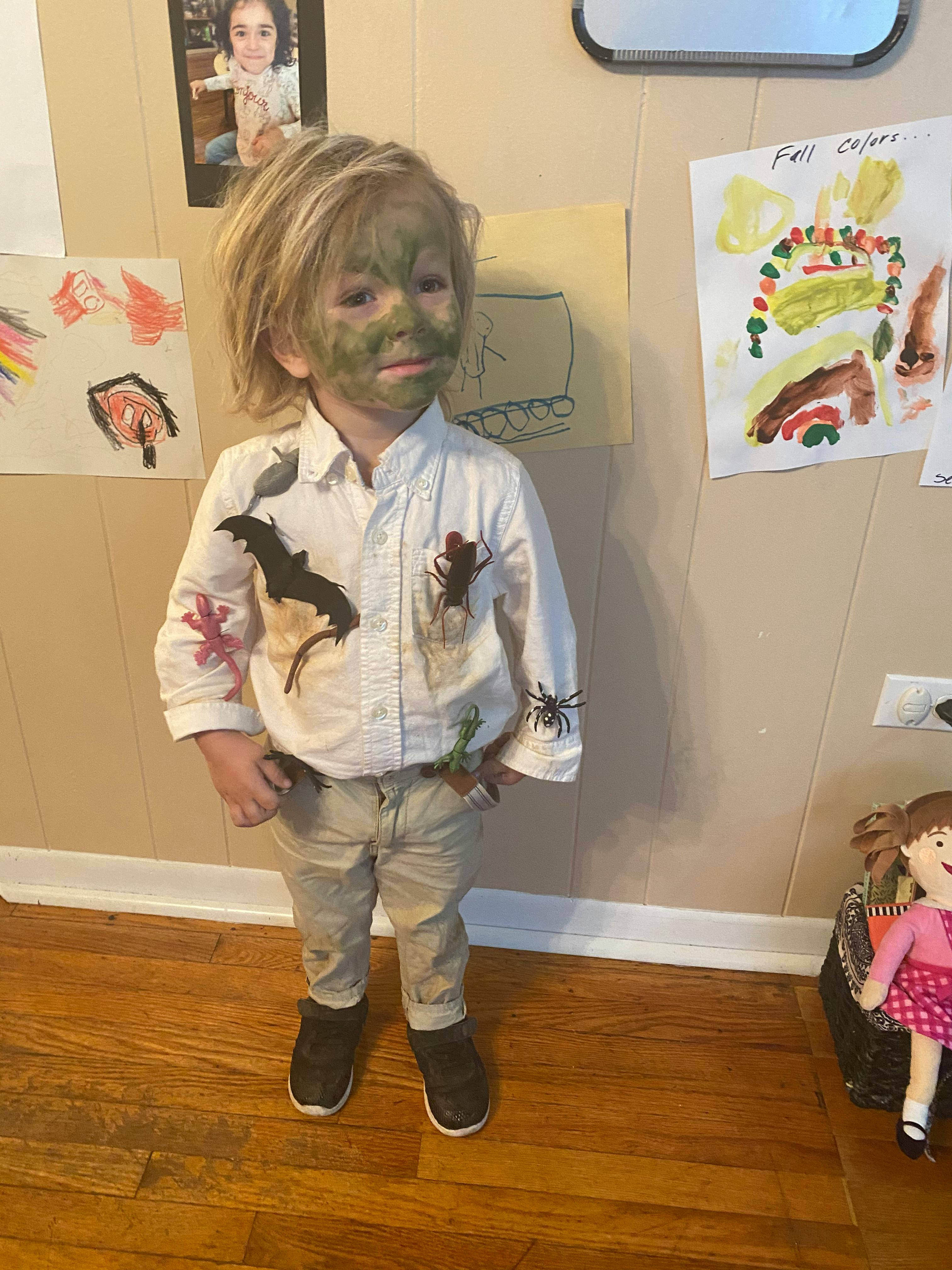 Child with green face paint and a white shirt with toy insects and a bat