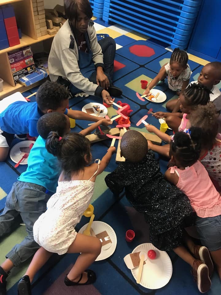 Adult and children sitting on a rug, engaged in an activity with craft sticks