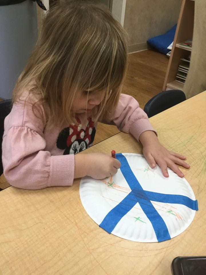 Child coloring on a paper plate with blue tape in a classroom