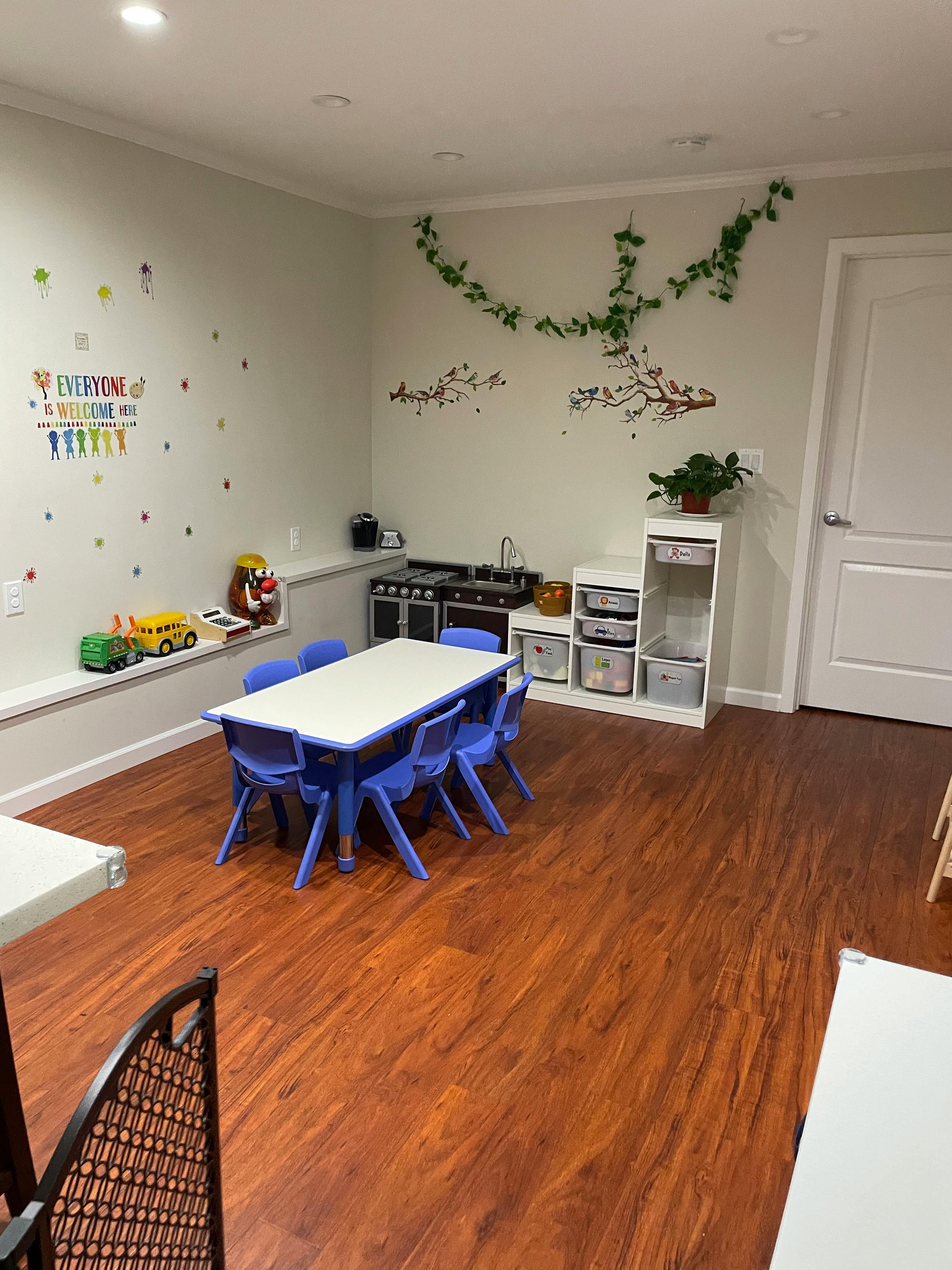 Children's classroom with small table and chairs, play kitchen, and wall decorations