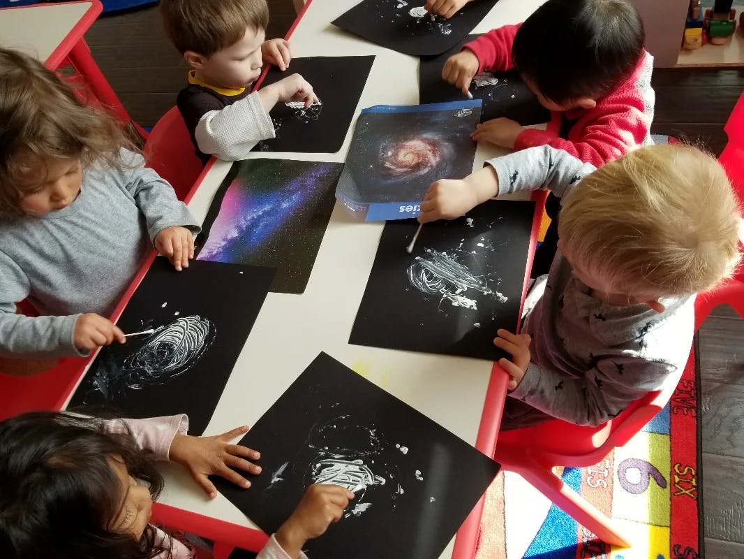 Children painting on black paper at a table