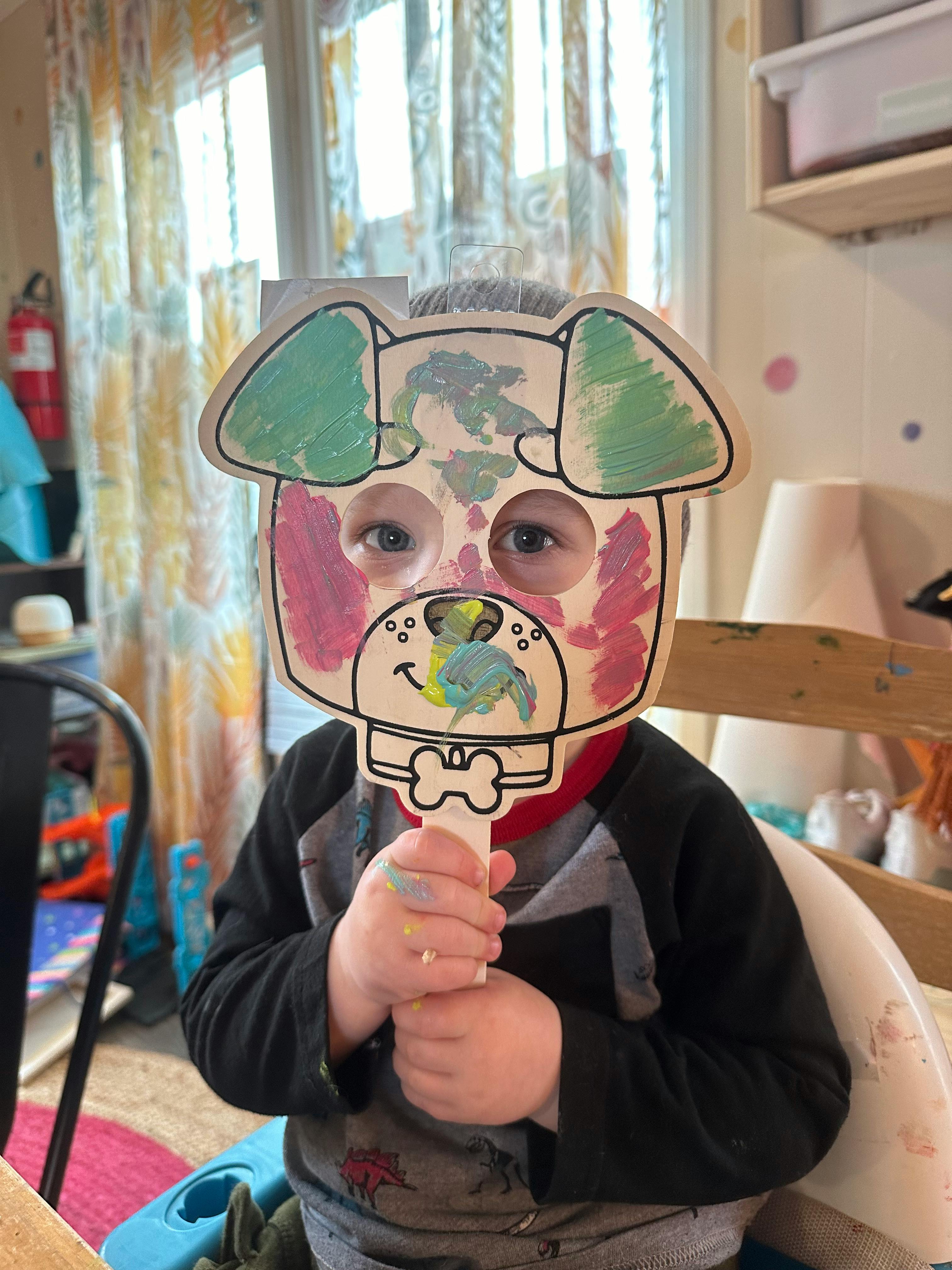 Child holding up a painted dog mask to their face