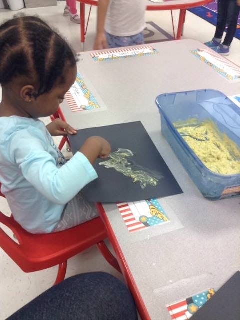 Child creating art with glue and glitter on black paper