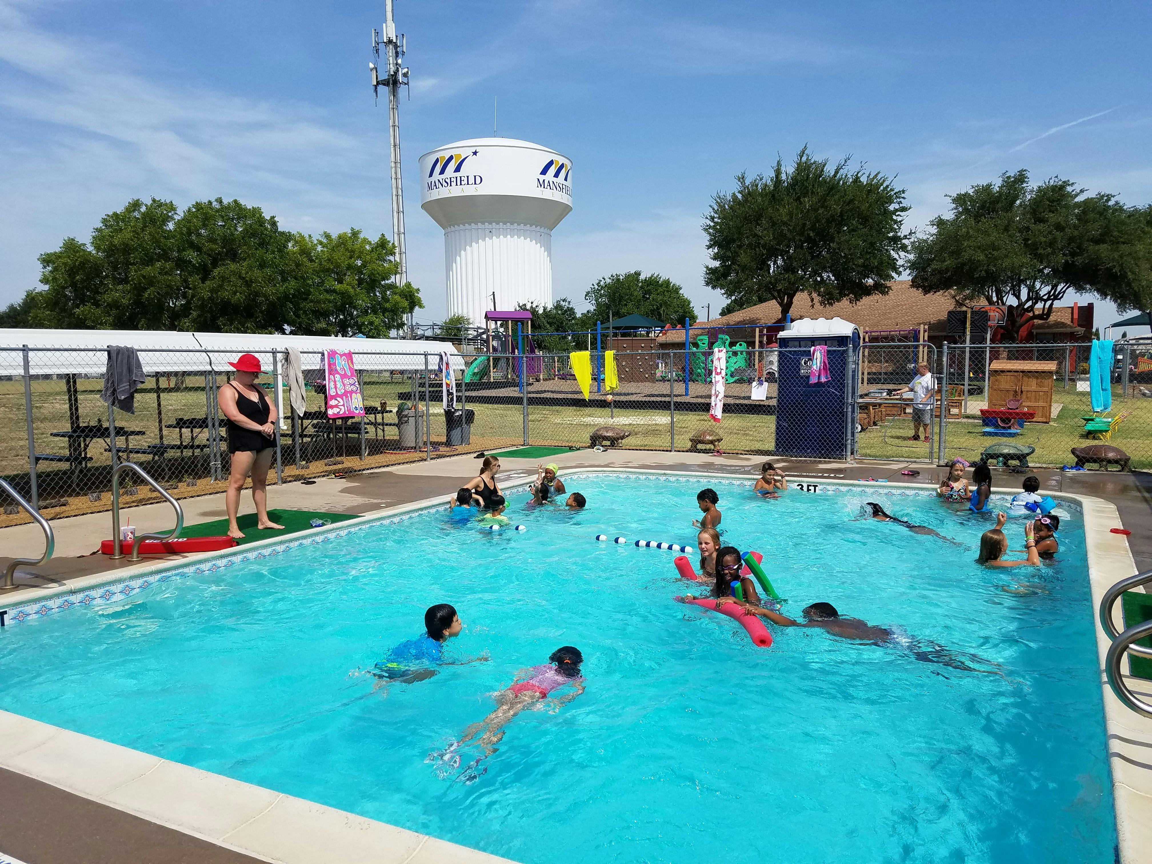 People and children swimming in a pool with a person standing by the pool