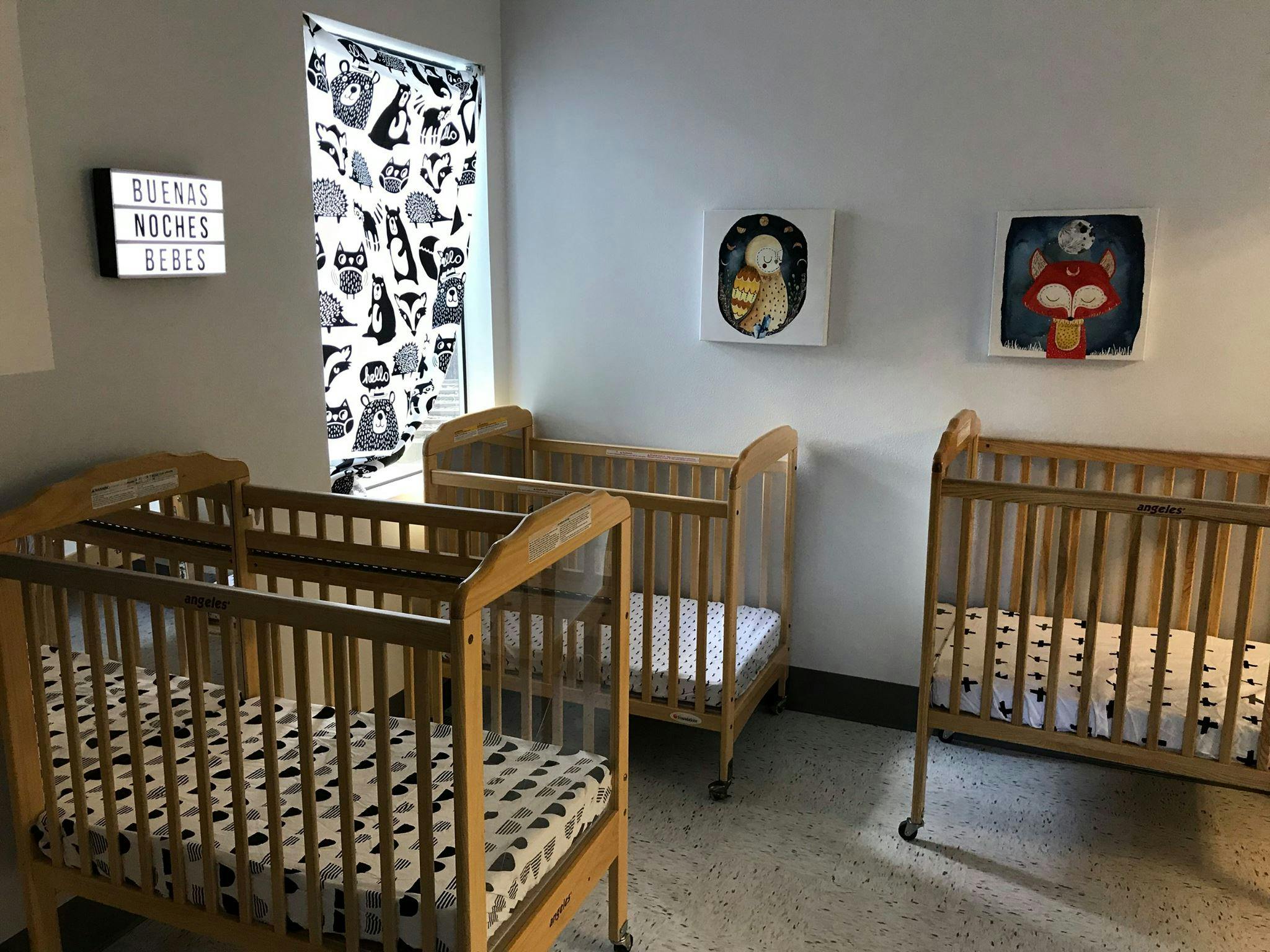 Three empty wooden cribs in a room with wall art