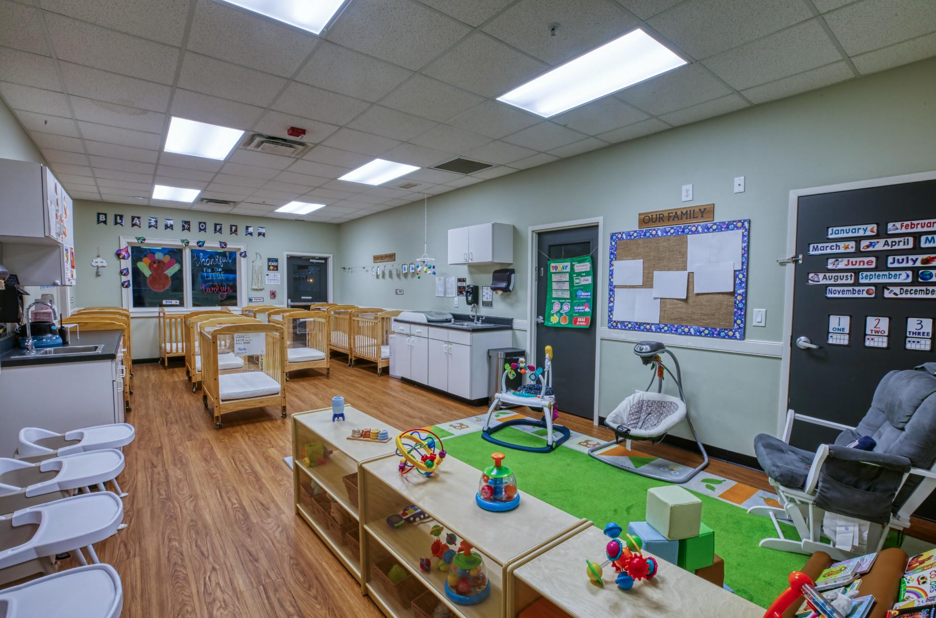 A classroom with cribs, play mats, toys, and baby equipment