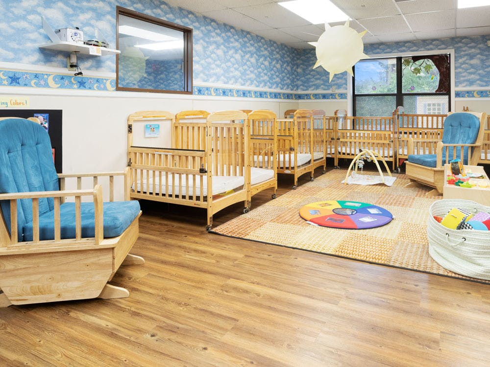 A childcare room with multiple cribs, a rocking chair, and play mats