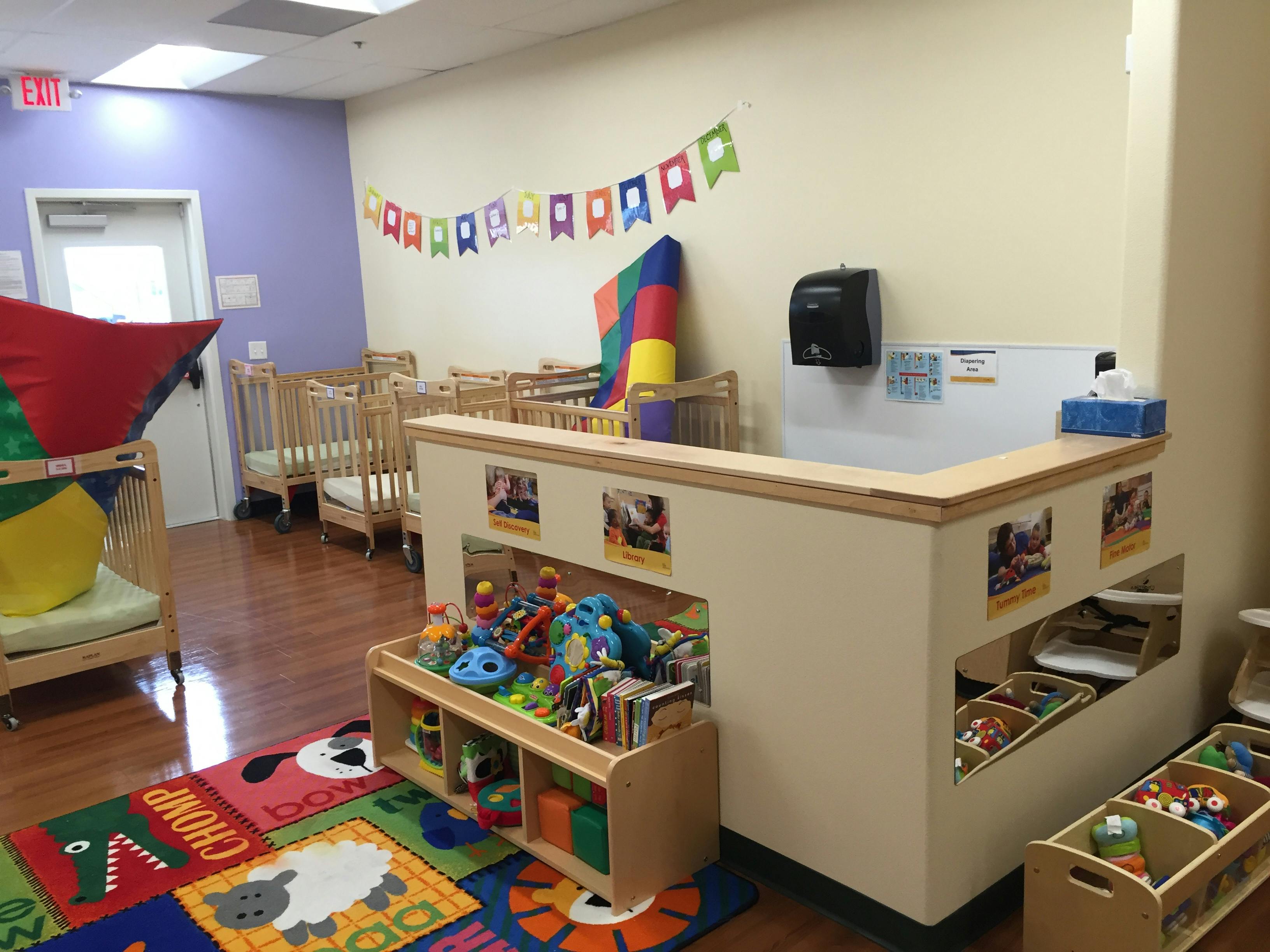 Daycare room with cribs, colorful rug, and toy storage