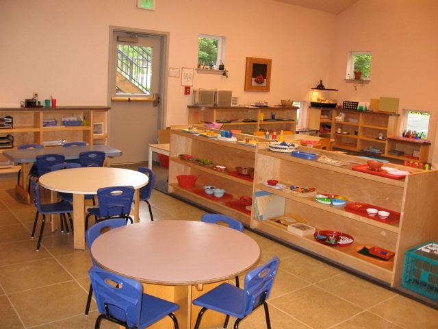 Classroom with small tables and chairs, shelves with learning materials