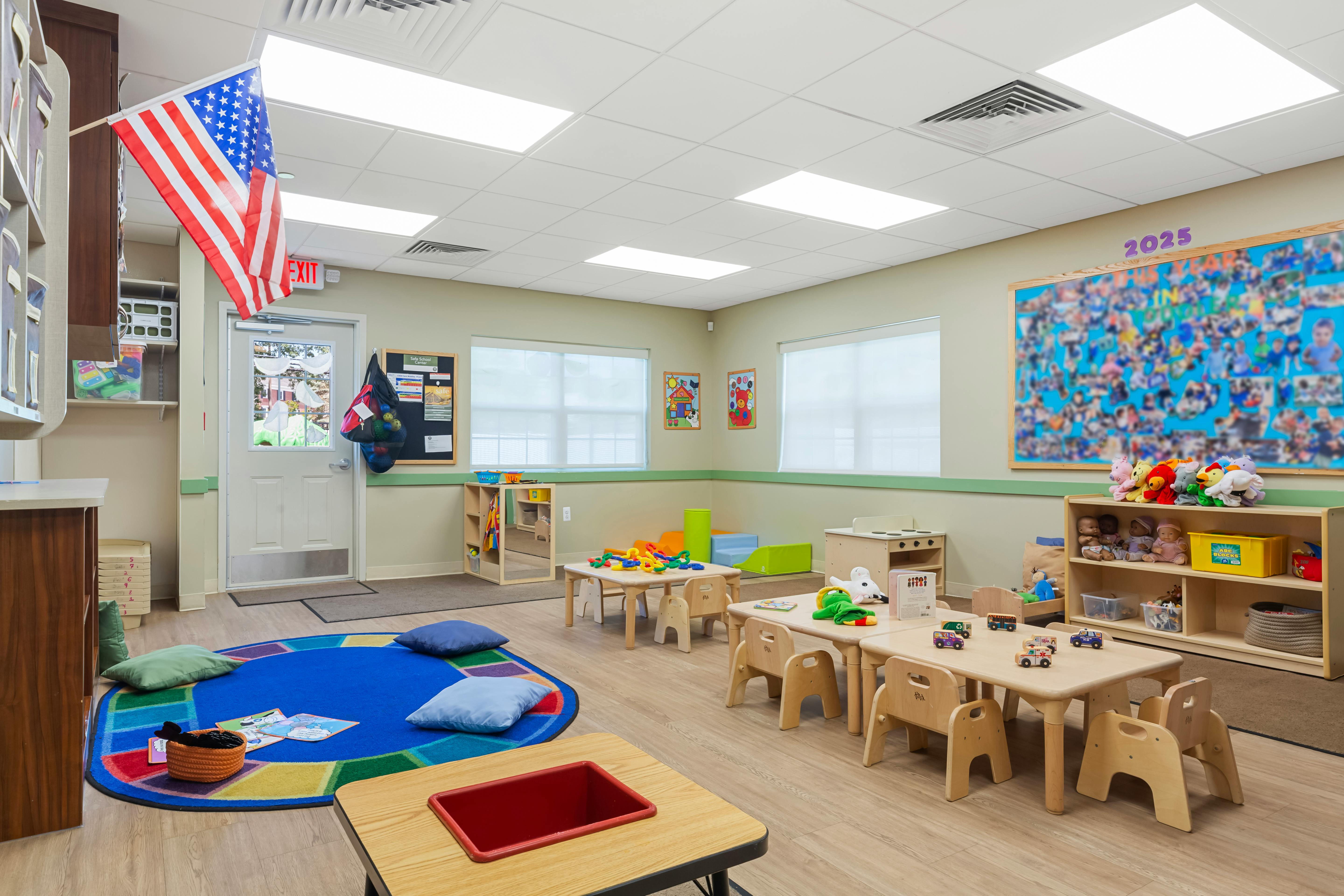 A classroom with small tables and chairs, toys, and an American flag hanging