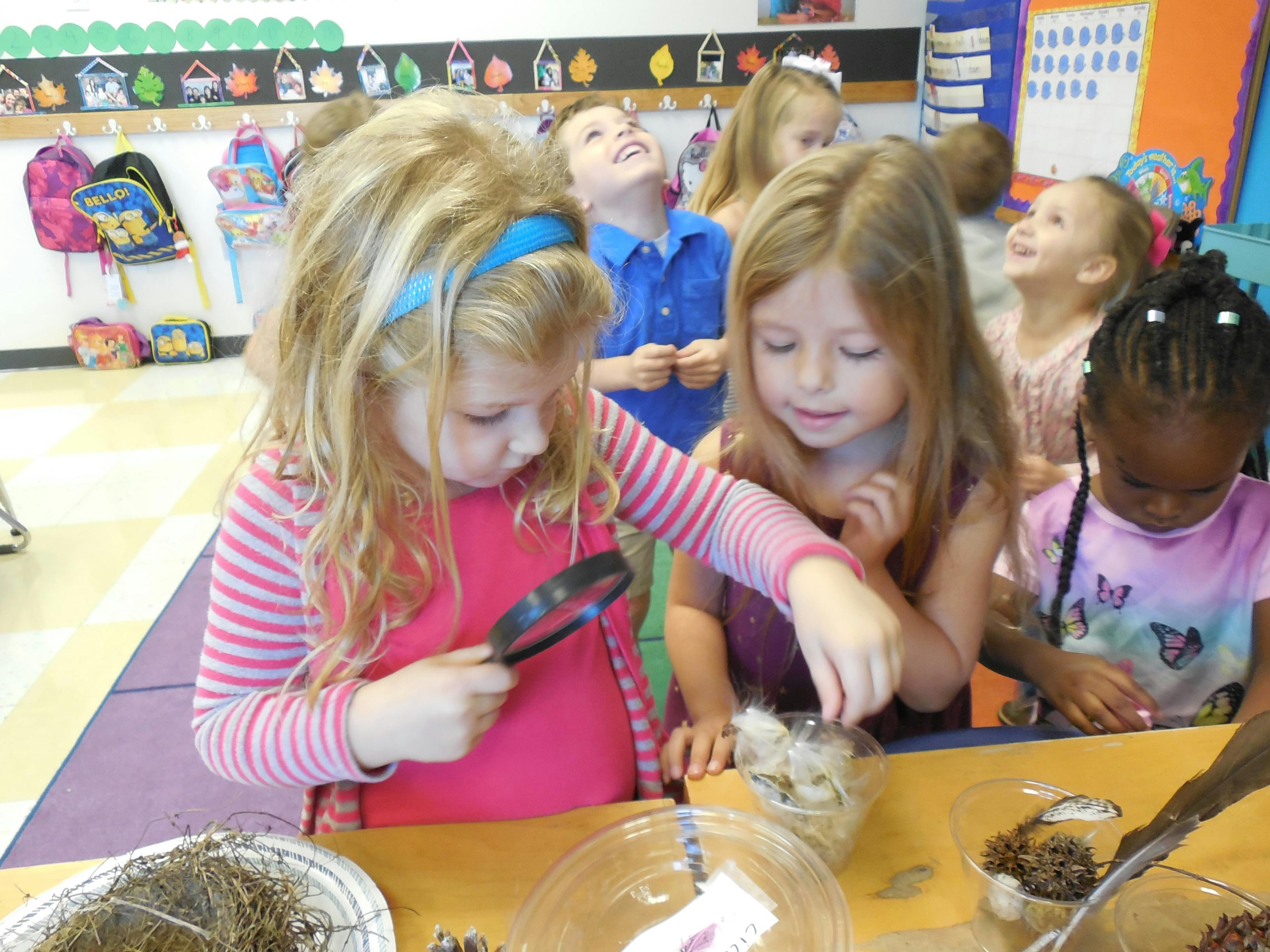 Children in a classroom examining items with a magnifying glass