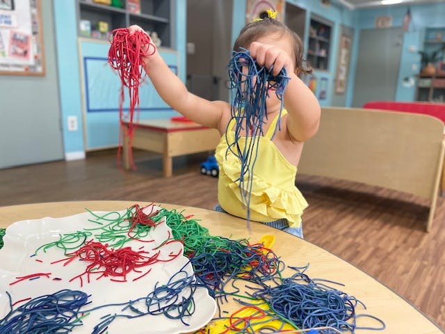 Child holding red and blue yarn over a table with more yarn