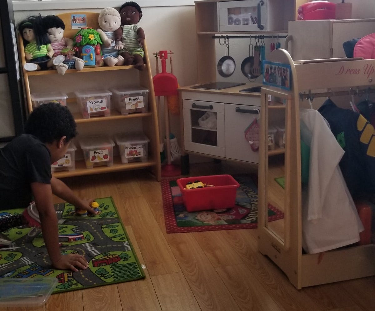 Child playing with a toy car on a rug in a classroom