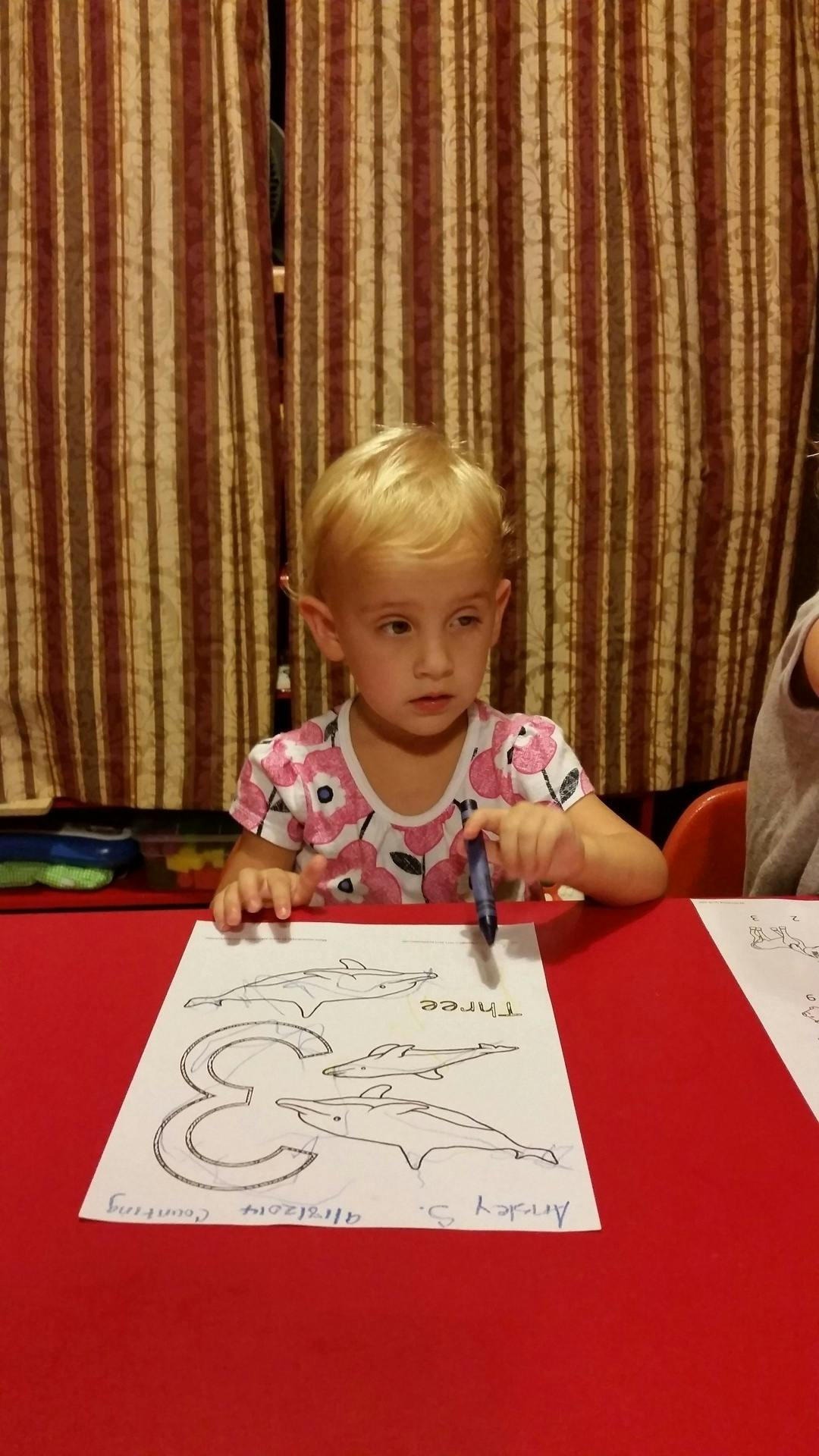 Child coloring a picture of dolphins and the number three